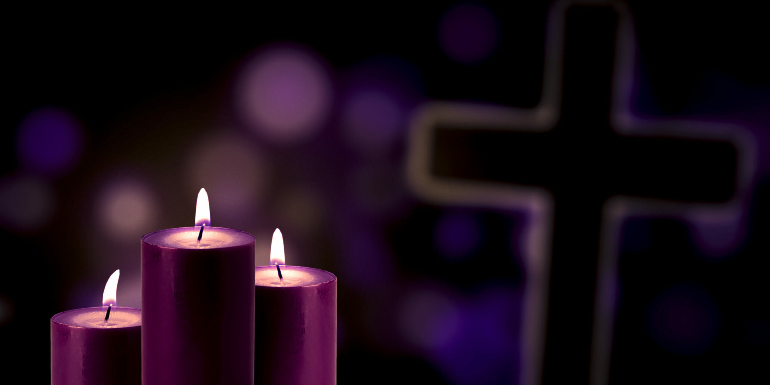 Picture of three purple candles glowing with a cross symbol and bokeh background